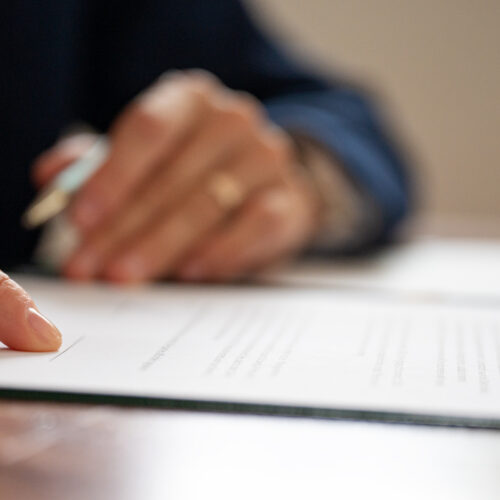 Low angle closeup view of businessperson or lawyer pointing to a signature line at the bottom of legal document or contract.
